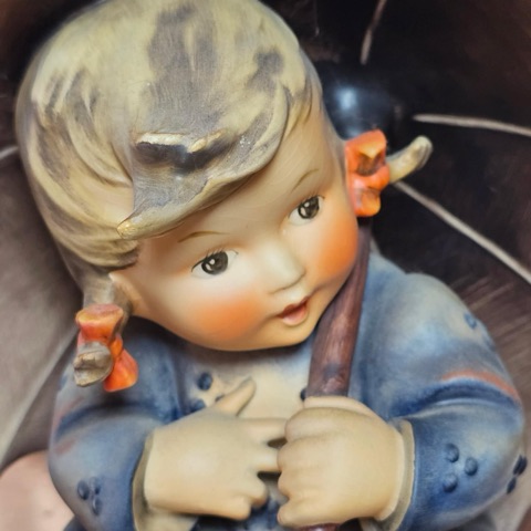 Close-up of the Umbrella Girl figurine&rsquo;s face, with wind-blown hair, orange hair bows and rosy cheeks, holding her umbrella handle.