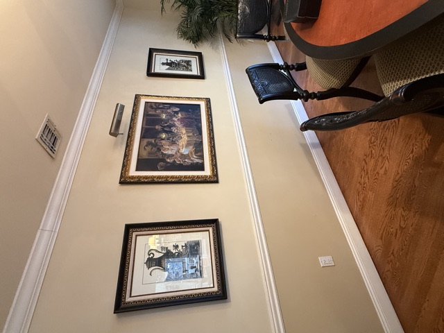 Three framed artworks hung along a cream dining room wall above a chair rail, with black cane-back dining chairs and a round wooden table in the foreground.